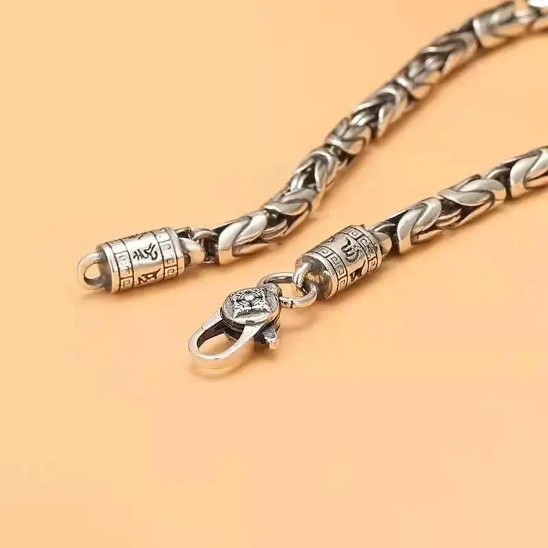Silver chain necklace with intricate design on a beige background